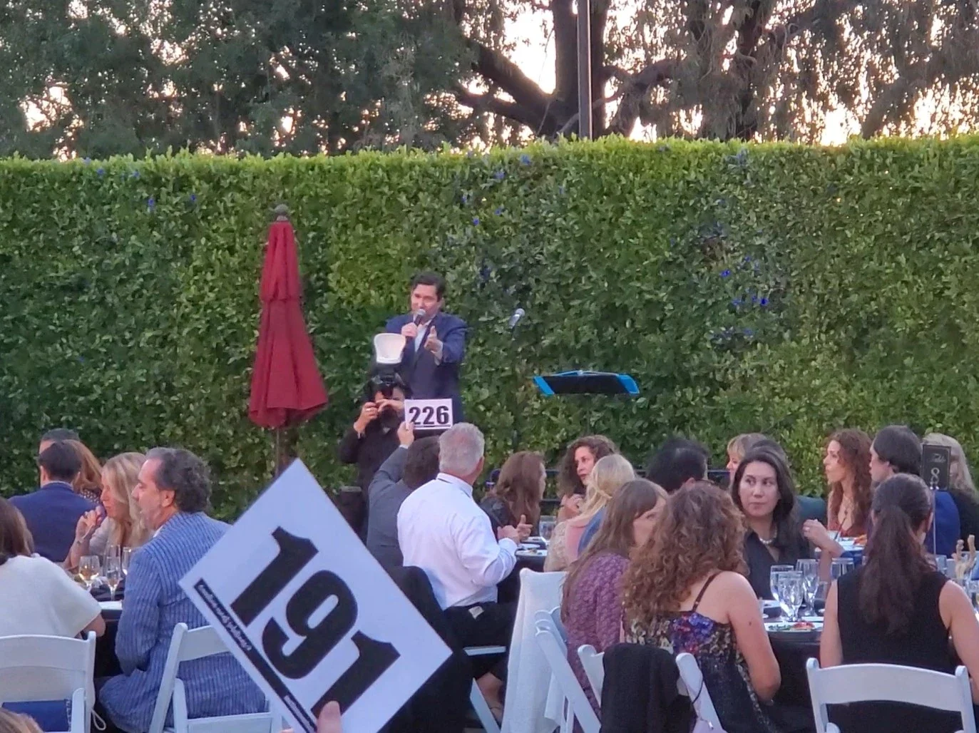 A male auctioneer takes bids from a seated crowd.